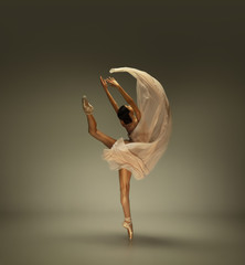 Graceful classic ballerina dancing, posing isolated on grey studio background. Tender beige cloth. The grace, artist, movement, action and motion concept. Looks weightless, flexible. Fashion, style.