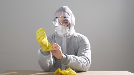 Man in protective suit putting or takes off on protective gloves. Man puts on a protective gloves. Portrait of the man in protection suit. Epidemic situation. Covid-19 