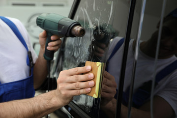 Naklejka premium Worker tinting car window with foil in workshop, closeup