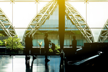 The silhouette of tourists next to th big glass windows with the flare from the outside in the sunny day. 