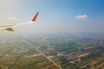 The part of airplane wing with the naturescape with sky clouds and buildings on the ground while flying. 