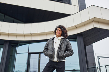 Handsome young man with curly black hair posing for the camera on the street against building