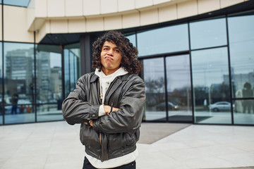 Handsome young man with curly black hair is on the street against building