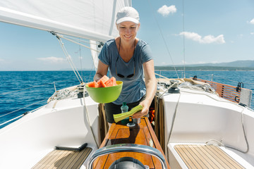 Woman on the deck of a sailboat serving fresh watermelons. Sailing and yachting concept.
