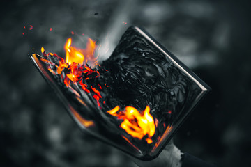 A black-and-white image of a man holding an old book in his hand, which is burning with a bright red flame. - obrazy, fototapety, plakaty