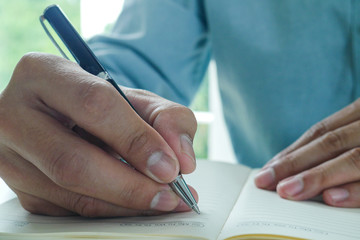Image of male hand focusing holding a pen to write.  Businessman writing on paper report in office.