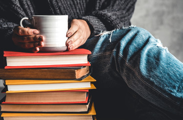 Stack of books with mug on top in front of woman reading book, education, training, hobbies