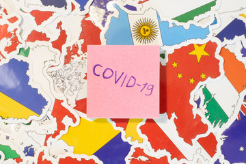 Paper with word Covid-19 flat lay top view on background with many national flags of countries. Concept of world healthcare problem with virus Coronavirus