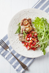 Grilled Pork Tenderloin with Tomato Salsa and Arugula. White wooden background. Top view.