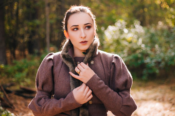 A girl stands in a dark forest, in a brown coat with a red belt and boots. Slovenian girl.