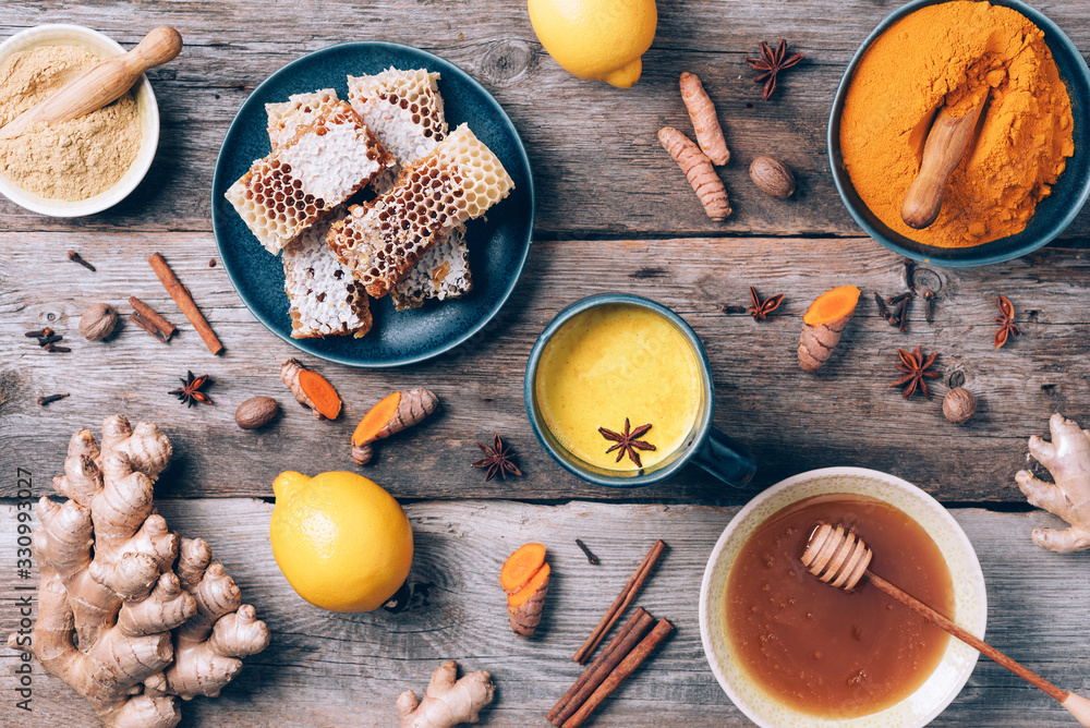 Wall mural yellow turmeric latte drink. golden milk with cinnamon, turmeric, ginger over grey background. top v