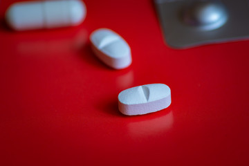 White pills of the medicine lie on a red table in close-up