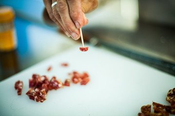 A close up selective focus shot on the hand of a person using a cocktail stick to sample pancetta cured meat at a butchers counter at farmers market.