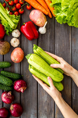 Pick vegetables. Squash in hands near autumn harvest on wooden background top-down