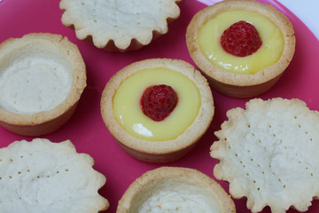 Tartlets with lemon Kurd. Decorated with raspberries. Lie on a plate. Next to them are tartlets without toppings.