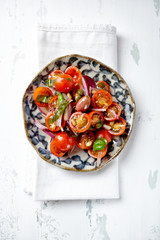 Healthy salad with cherry tomatoes, kalamata olives, red onion and capers. Bright wooden background. Top view. 