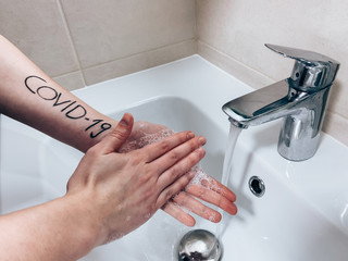 Hands of woman(palms,fingers,forearms) with inscription “COVID-19” are washing in...