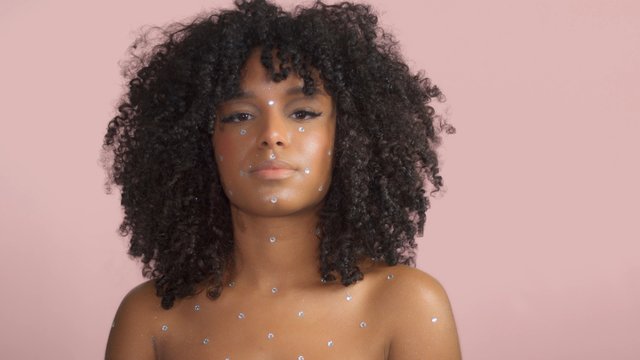 Mixed race black woman with curly hair covered by crystal makeup on pink backgroundinfluencer stylized makeup