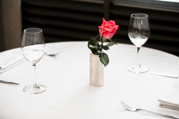 White table with glasses and cutlery. Empty restaurant table with red rose.