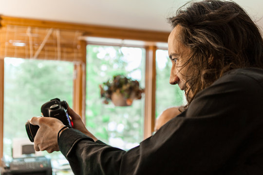 A close up and side profile of a professional male photographer concentrating on framing a shot indoors, holding a DSLR camera in hands with copy space.