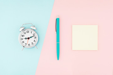 Metal vintage alarm clock with office pen and yellow sticky notes on colorful paper background....