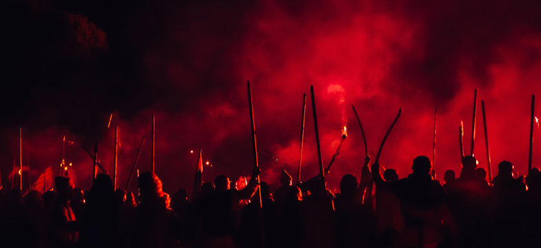 A medieval troop on the battlefield at night. Silhouettes of the fighting medieval soldiers on the red foggy background. Rebels during a riot with torches at night.
