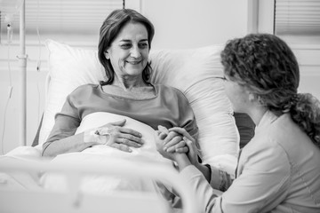 Smiling elderly woman and caring daughter holding her hand in the hospital, black and white photo