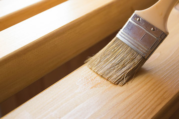 Paint coating and protection of wooden surfaces.Brush that covers wooden planks and beams with varnish for interior work in the color of oak. - obrazy, fototapety, plakaty
