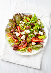 Healthy salad with feta cheese, various olives, leek and tomatoes. White wooden background. Top view. 