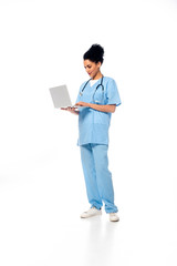 Full length view of african american nurse with stethoscope using laptop on white background