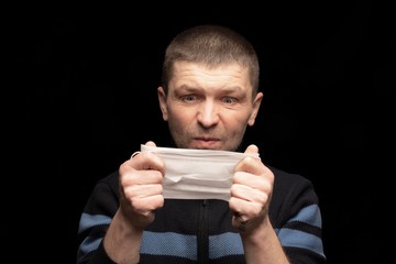 an adult man looks at a protective medical mask , and does not understand why to put it on ....