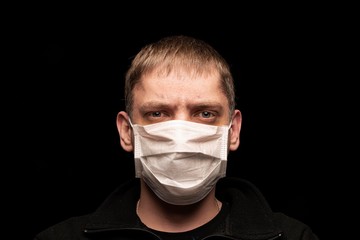 A sick male patient in a protective medical anti-bacterial mask looks intently at the camera, afraid of an epidemic and a pandemic. He worries about his health and doesn 't Fear and panic