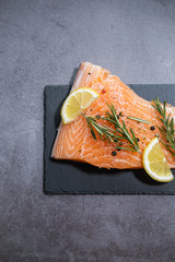Raw salmon fillet with lemon slices on slate plate and concrete background. Vertical view.
