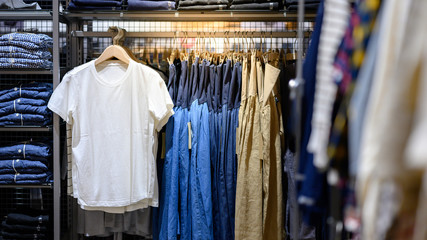 White T-shirt hanging on rack in clothes shop with shirt and dress beside. Summer collection...