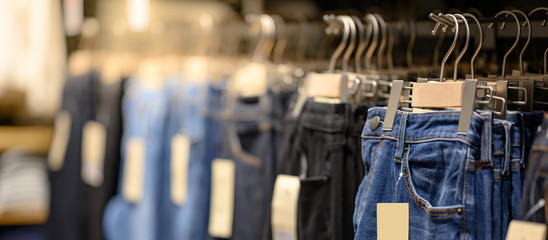 Jeans or Denim pants (trousers) hanging on rack in clothes shop. Fashion product collection in clothing store for selling. Textile industry and business concept - obrazy, fototapety, plakaty