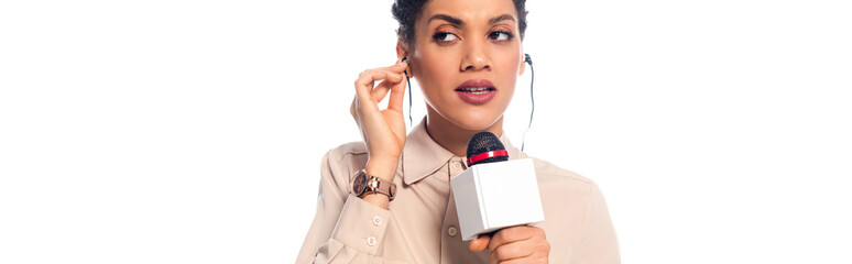 African american journalist with microphone putting headphones in ears isolated on white, panoramic shot