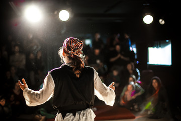 A selective focus view from behind an actor dressed in pirate costume, performing on stage to a...