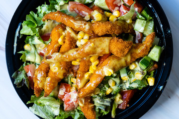 Take Away Healthy Cajun Salad with Chicken Fingers and Mustard Sauce in Black Plastic Plate Box / Package.
