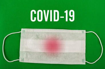 Medical protective mask on green background with Covid-19 text.