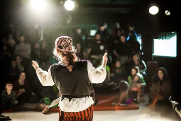 Foto op Aluminium A performing arts entertainer is seen from the back in selective focus, dressed as a pirate on stage during a comedy act with blurry audience at back. © Valmedia
