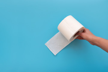 Hand holding toilet paper rolls on blue background. Copy space