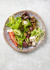 Healthy salad with feta cheese, various olives, leek and tomatoes. Bright wooden background. Top view.