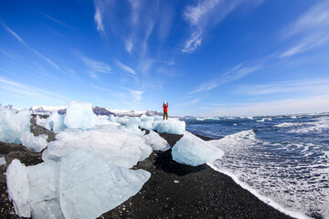 A man on a block of ice on the black volcanic sand on the "Diamond beach" in Iceland