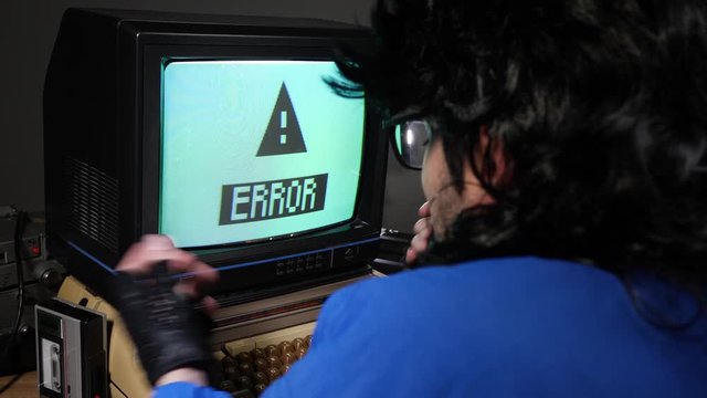 Upset, mad retro computer geek getting frustrated  and hitting old concept computer from 70s 80s because of a flashing error sign..