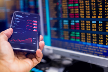 Red graph on smartphone with blurry computer monitor showing stock price slump. The concepts of the...