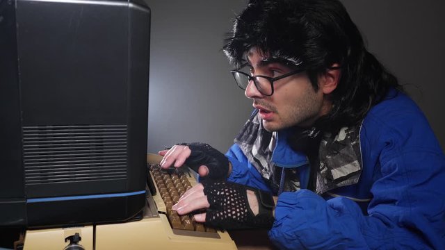 Concentrated retro nerd in glasses from the 70s 80s, typing while using an old computer. Vintage technology concept.