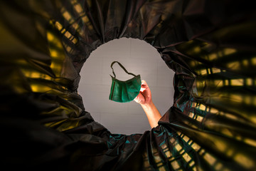 Throwing a face mask into the trash. With a worm view from the inside of the trash bin.
