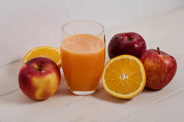 A glass of freshly squeezed apple-orange juice with fresh fruits on a white wooden background. Healthy food, proper breakfast. Raw food diet