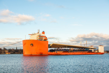 Seascape side view of a large orange semi-submersible heavy-lift ship with large load entering harbor in Stockholm Sweden.