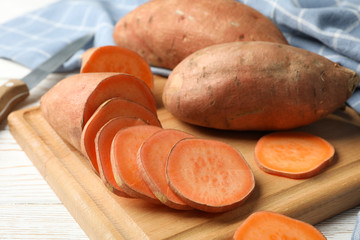 Sweet potato, knife, board and towel on wooden background, close up